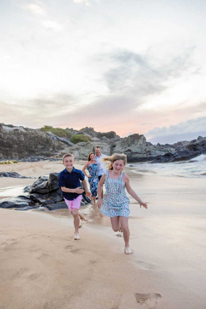 Candid moment of all four family members smiling and looking at each other with ocean waves behind them