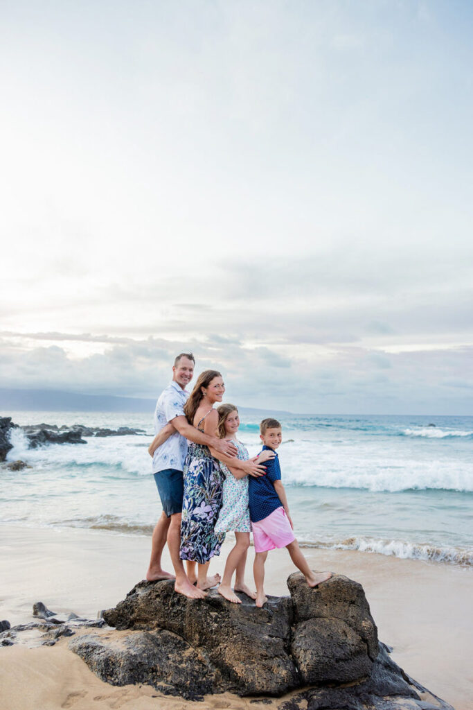 Parents hugging on the lava rocks with waves crashing behind them