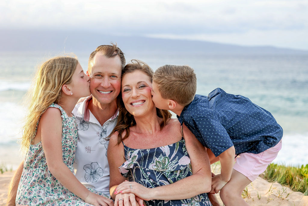 Candid moment of all four family members smiling and looking at each other with ocean waves behind them