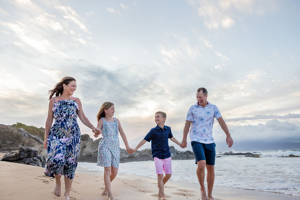 Family of four walking hand in hand along the beach at sunrise in Maui
