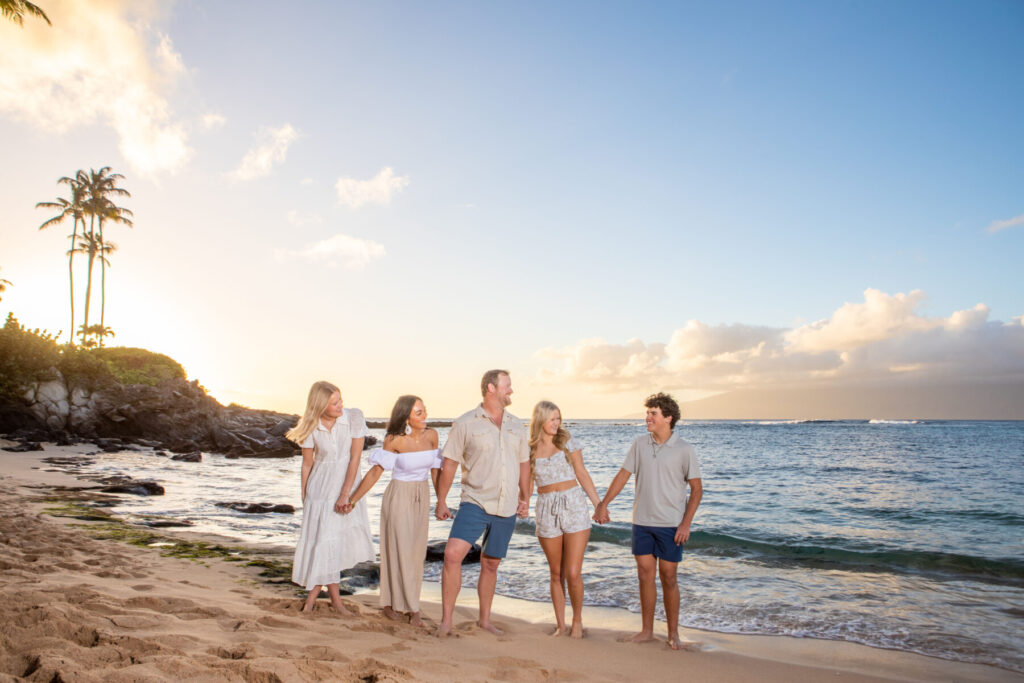 Family holding hands along Kapalua Bay shoreline during golden hour in Maui