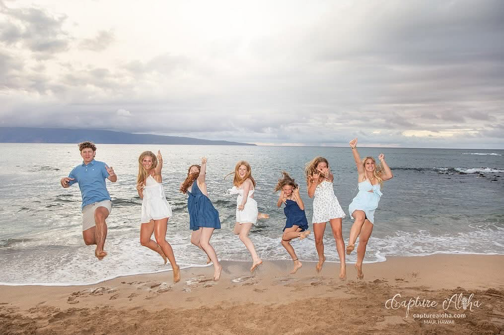 Maui family photos – a group of teens and kids jump together at the waterline, ocean horizon and soft evening light capturing carefree energy in Maui.