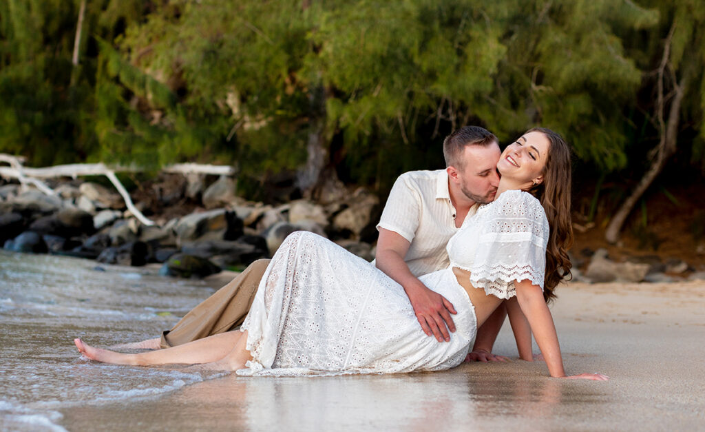 Playful kiss during a Maui couple photo session at DT Fleming Beach, sitting barefoot in the ocean at sunset.