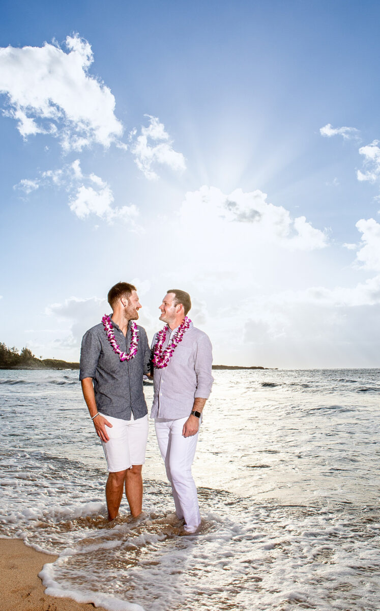 Golden Maui couple photo session at sunset, couple holding hands in the ocean with vibrant skies behind them.