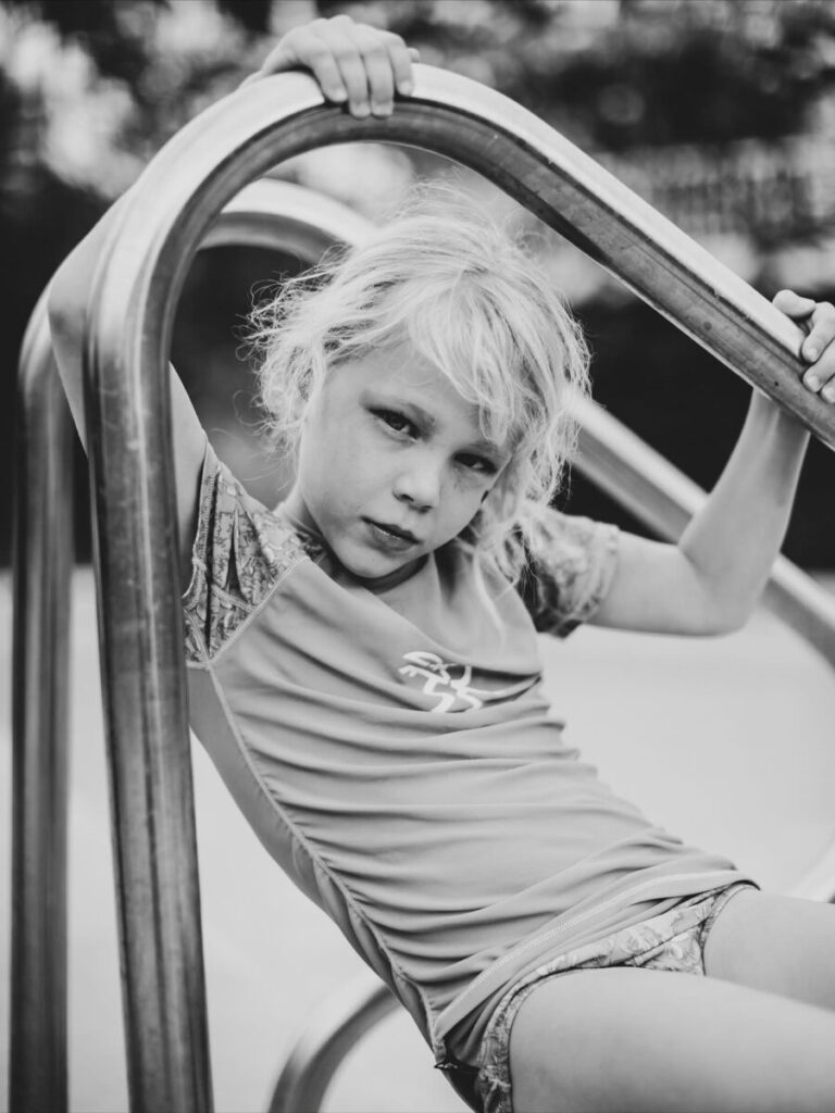Black-and-white Maui portrait – close-up of a child leaning on pool rails, thoughtful expression and soft light for a timeless, candid feel in Maui.