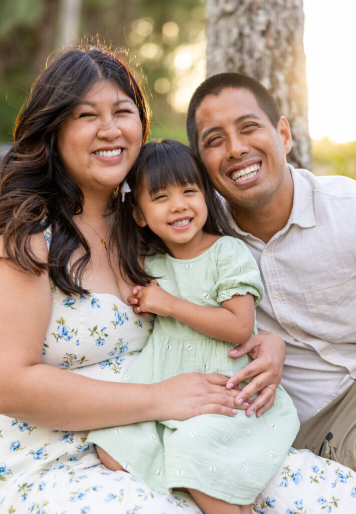 Maui family photography at DT Fleming Beach – parents hugging daughter and smiling during sunset on the west side of Maui.