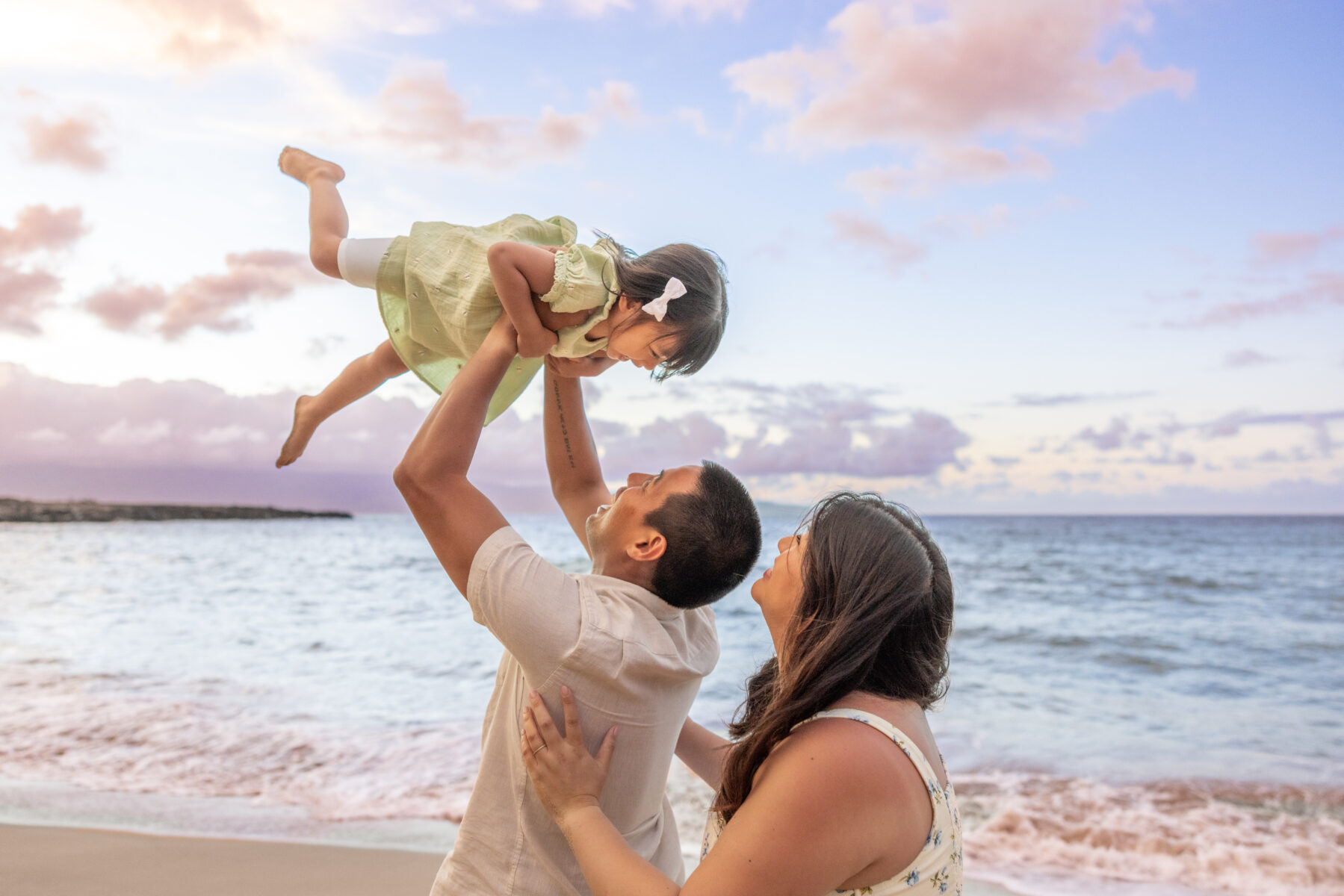 Father lifting daughter into the air against a pink sunset sky during Maui family photography session on the west side of Maui.