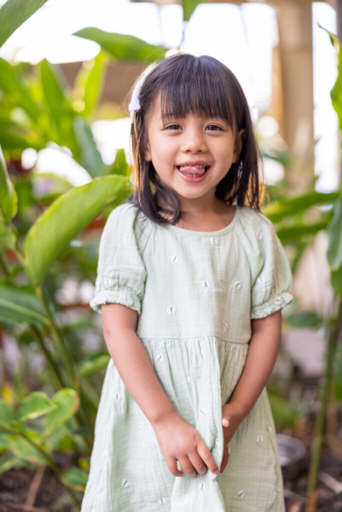 Little girl smiling in green dress during Maui family photography session surrounded by tropical plants at DT Fleming Beach.