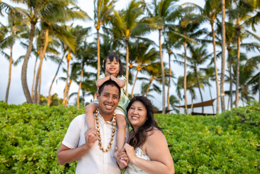 Family of three smiling together under palm trees during Maui family photography session on the west side of Maui.