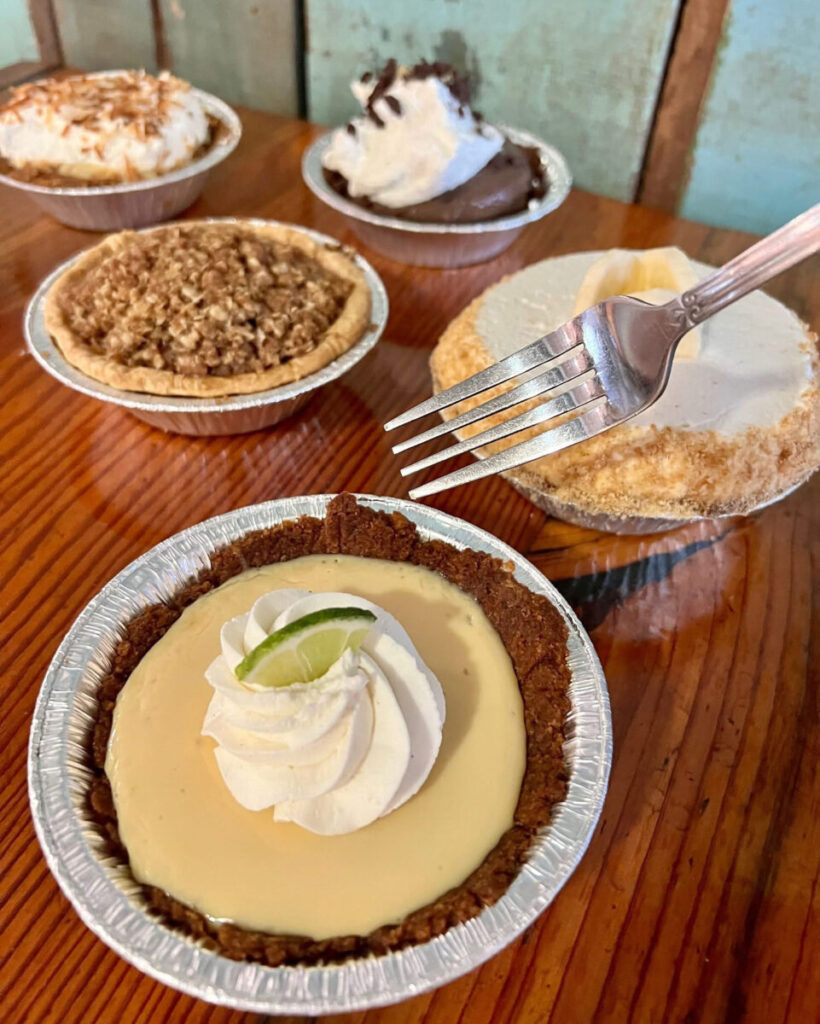 Assorted fresh mini pies with whipped cream and flaky crusts displayed on a rustic wooden café table at Leodas