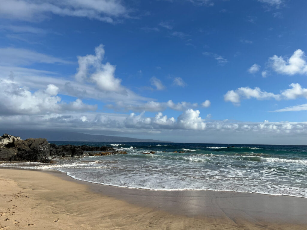 Peaceful shoreline view with turquoise water, black lava rocks, and soft white clouds over the horizon at ironwood's beach