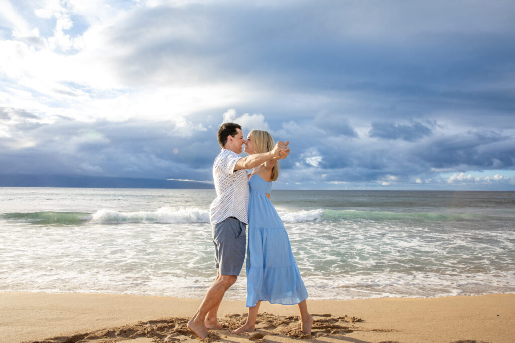 Couple dancing on the beach beneath a dramatic cloudy sky at DT Fleming Beach, highlighting why it’s one of the Top Maui Photoshoot Locations for couples.