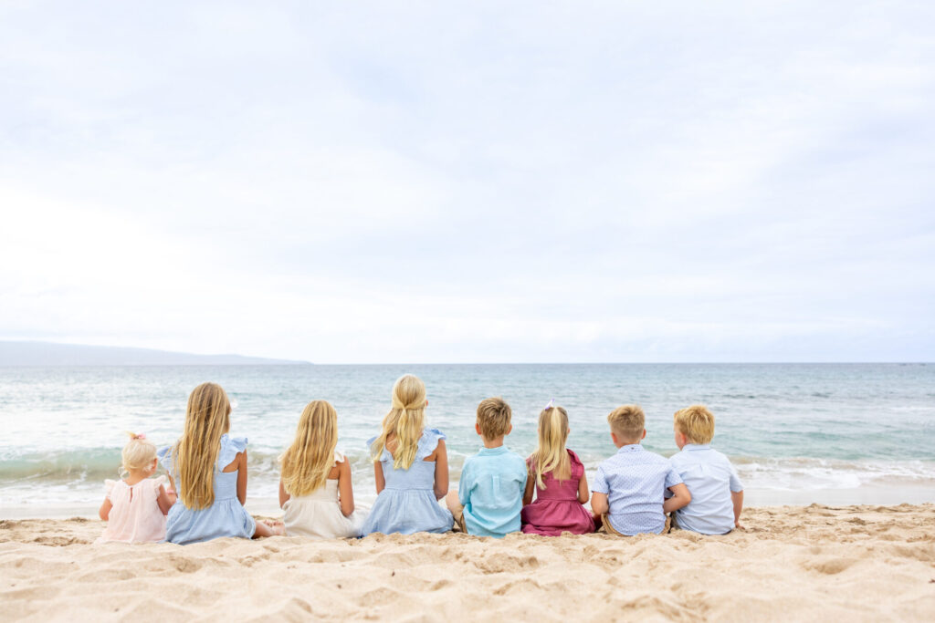Children sitting side by side in the sand looking out at the ocean at DT Fleming Beach, one of the Top Maui Photoshoot Locations for large family sessions.