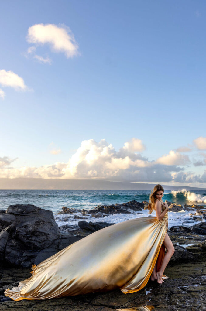 A woman wearing a bold red Hi Flying Dress posing confidently on Maui’s lava rocks, the long train sweeping in the wind.