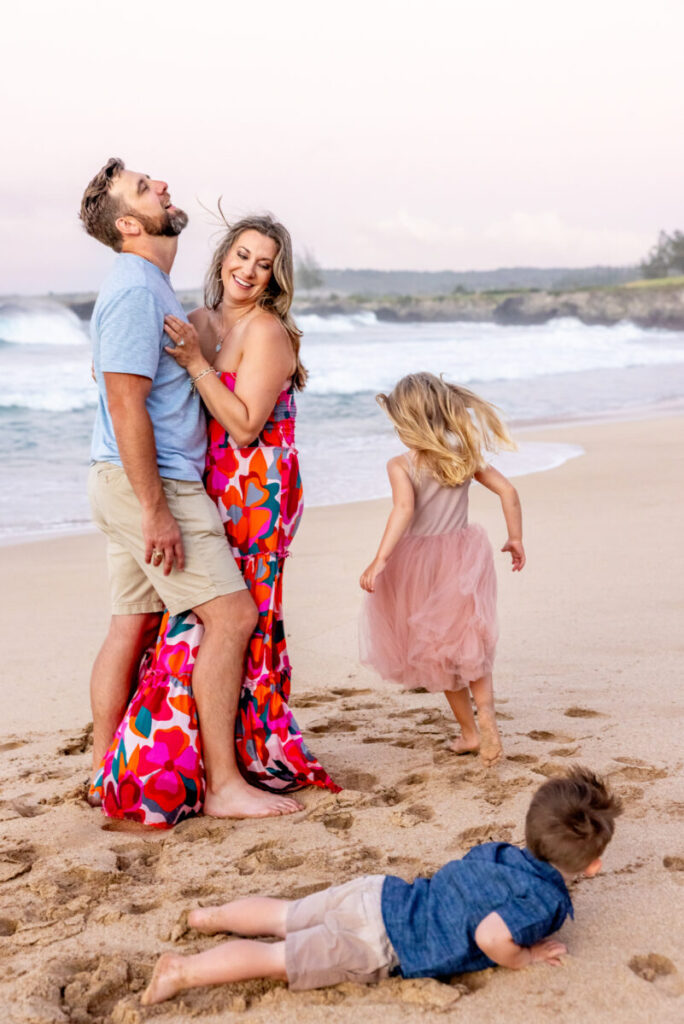 Maui Kids Photography session capturing a playful family moment on a sandy West Maui beach, with parents laughing while their children run and explore