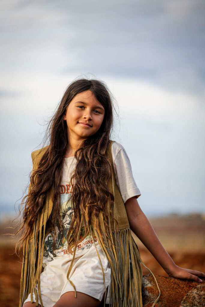 Maui Kids Photography portrait of a young girl standing outdoors at sunset, showcasing natural light, soft expression, and Maui’s warm, earthy scenery.