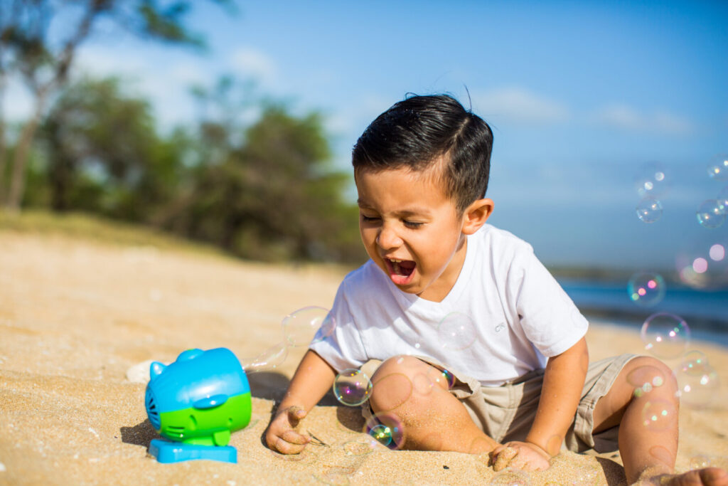 Maui Kids Photography candid of a toddler laughing and playing with bubbles on a sunny Maui beach, capturing pure joy and natural childhood moments.