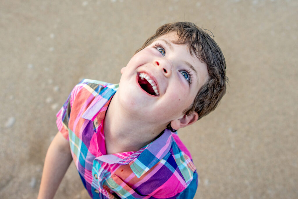Maui Kids Photography close-up of a young boy laughing and looking up with bright blue eyes during a beach session on Maui
