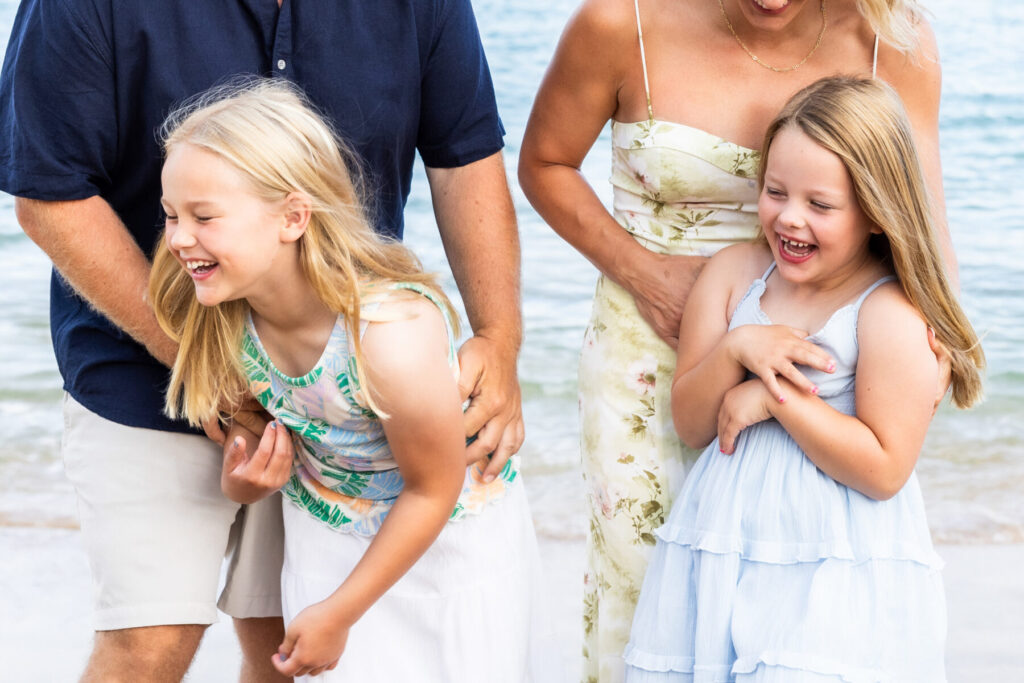 Maui Kids Photography candid moment of two young sisters laughing while their parents hold them during a joyful Maui family beach session.