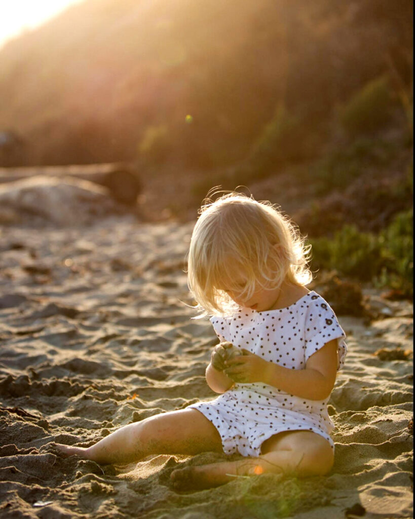 Maui Kids Photography natural candid of a toddler sitting in warm golden sand at sunset on Maui, playing quietly and exploring small details.