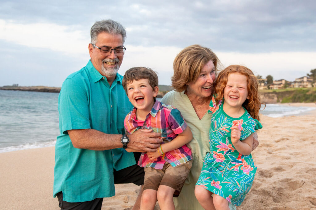 Maui Kids Photography joyful moment of grandparents holding their grandchildren during a Maui beach session, capturing genuine connection and family laughter.