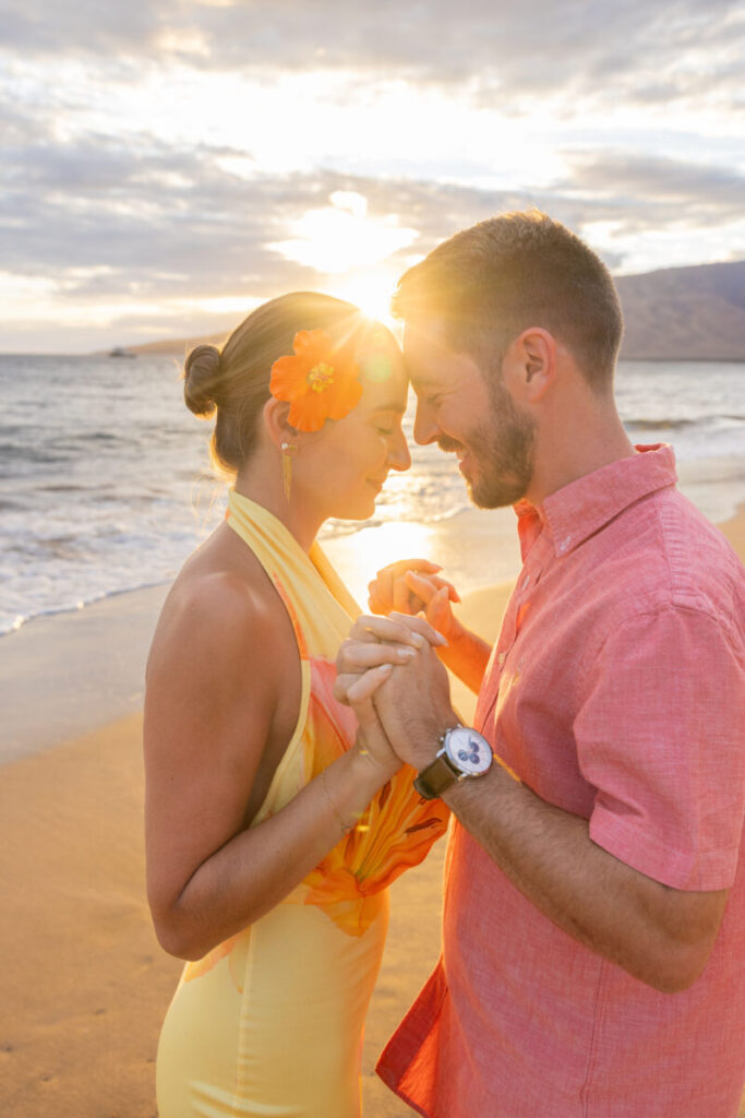 Maui surprise proposal at sunset as he kneels on the sand and she smiles in a white dress.