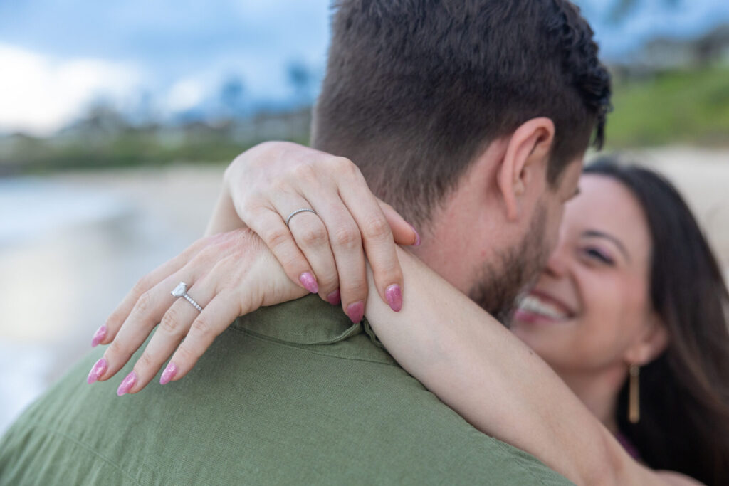 Maui surprise proposal close-up with the couple hugging and her engagement ring visible on the beach.