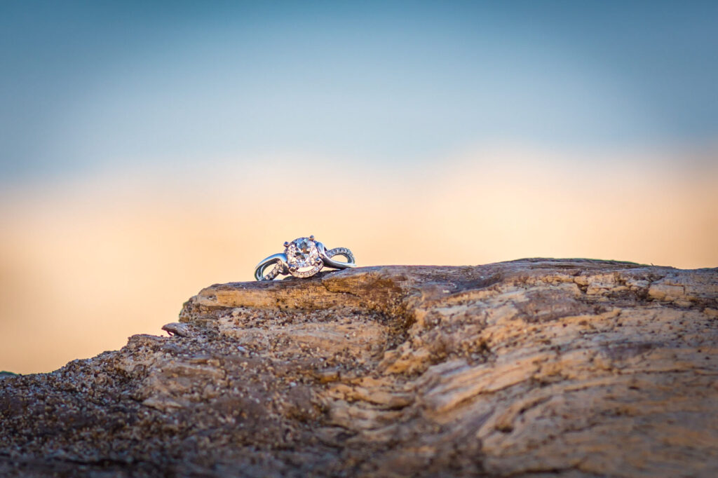 Maui surprise proposal ring detail photo with a diamond engagement ring resting on sunlit driftwood.
