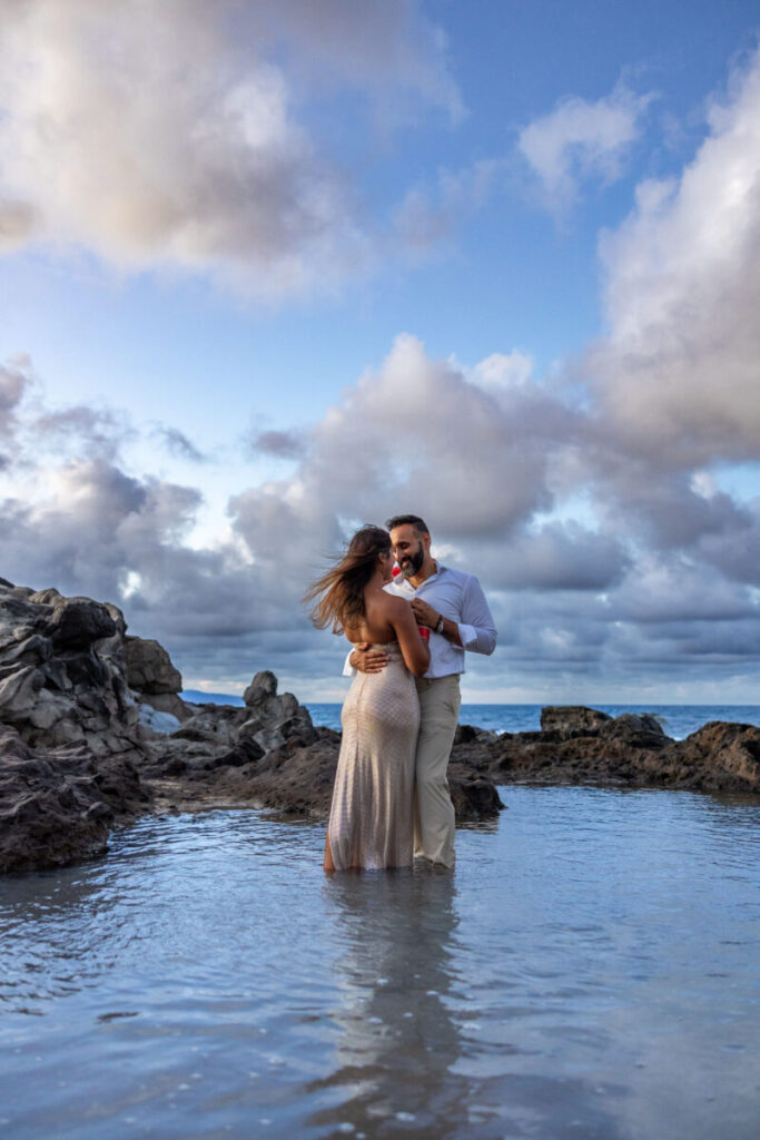 Maui surprise proposal couples session with the couple embracing in a tide pool under dramatic island clouds.