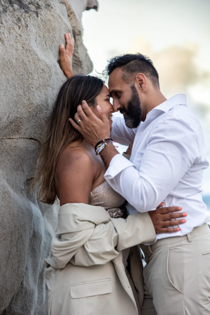 Maui surprise proposal couples session with an intimate hug and forehead touch beside a coastal rock wall.