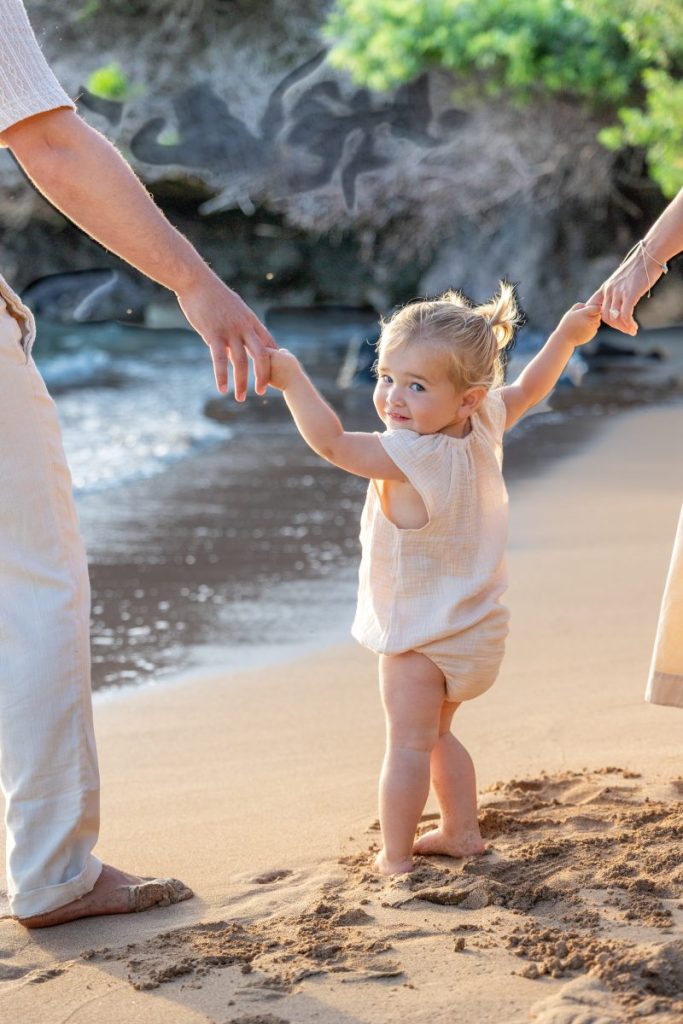 Maui family photoshoot capturing a toddler holding hands with parents while walking along the beach.