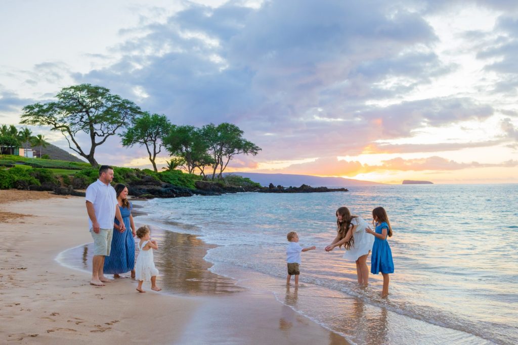 Maui family photoshoot at Maluaka Beach with parents and children playing at the shoreline during sunset.