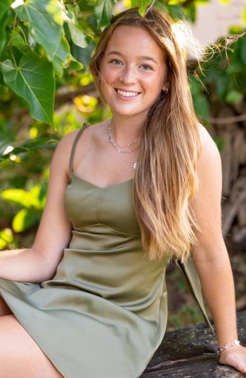 Senior girl sitting near greenery during a Maui portrait session.