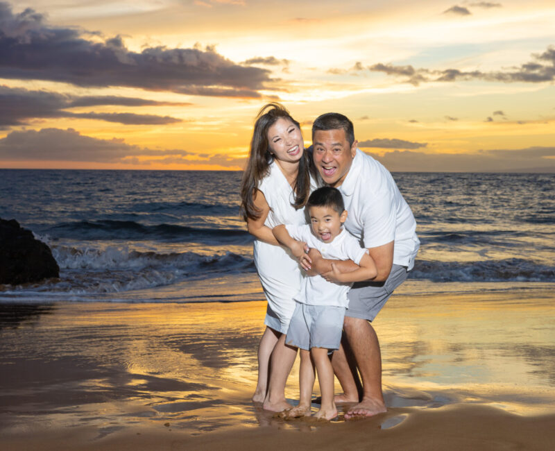 Family hugs at the waterline with glowing sky, Maui.