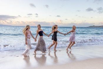 Group of friends holding hands and walking along the shoreline in Maui.