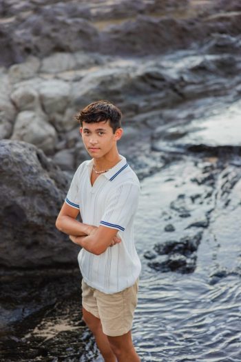 Teen boy standing near lava rocks on a Maui beach during senior portraits session.