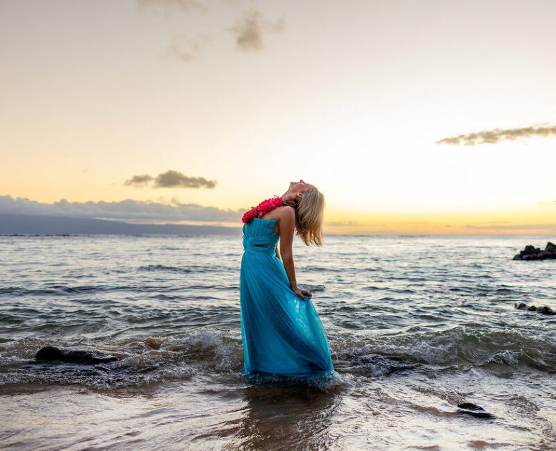 Senior Portraits in tide line, blue dress, lei and sunset glow, Maui coast.