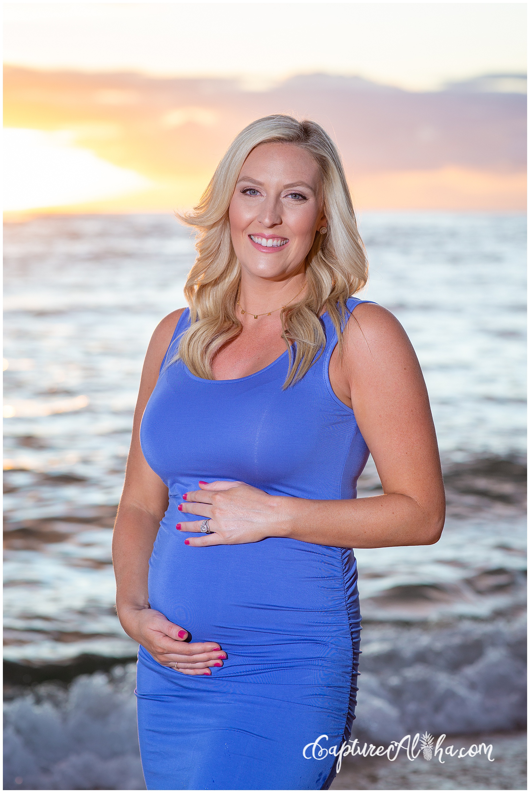 Pregnant woman on the beach in Maui wearing a blue dress during sunset