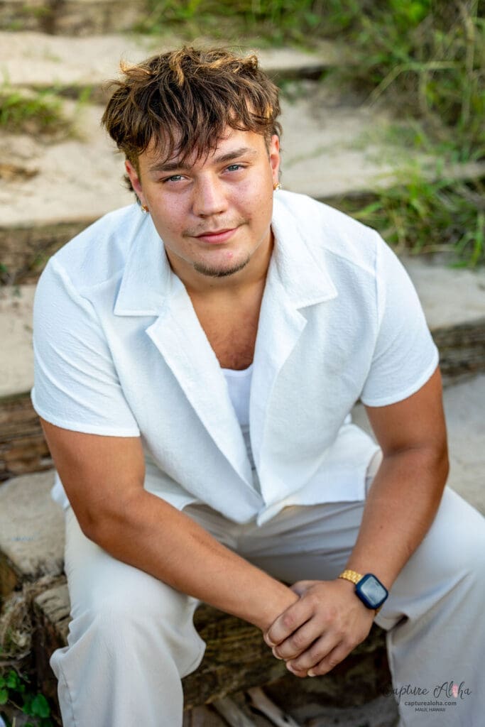 Senior portrait of a student in a scenic outdoor setting, standing confidently against a backdrop of nature. The student is dressed in a stylish outfit, with a relaxed yet confident pose. Soft, natural light highlights their features, while the surrounding landscape—whether it’s a beach, lush greenery, or distant mountains—adds depth and beauty to the image. The warm tones of the scene evoke a sense of calm and serenity, capturing the spirit of this special moment in time.