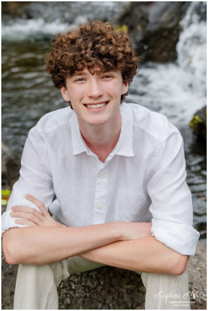 Senior portrait of a student in a scenic outdoor setting, standing confidently against a backdrop of nature. The student is dressed in a stylish outfit, with a relaxed yet confident pose. Soft, natural light highlights their features, while the surrounding landscape—whether it’s a beach, lush greenery, or distant mountains—adds depth and beauty to the image. The warm tones of the scene evoke a sense of calm and serenity, capturing the spirit of this special moment in time.