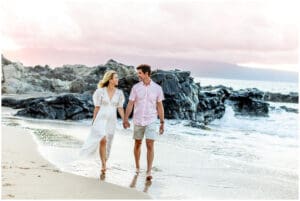 A loving couple embraces on a Maui beach during a romantic sunset photoshoot, with golden sand, gentle waves, and a breathtaking sky creating a dreamy atmosphere.