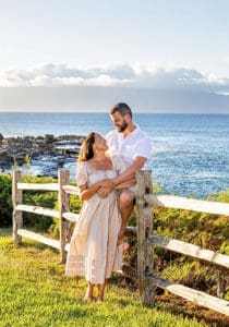 A loving couple embraces on a Maui beach during a romantic sunset photoshoot, with golden sand, gentle waves, and a breathtaking sky creating a dreamy atmosphere.