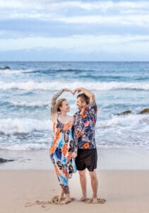 A loving couple embraces on a Maui beach during a romantic sunset photoshoot, with golden sand, gentle waves, and a breathtaking sky creating a dreamy atmosphere.