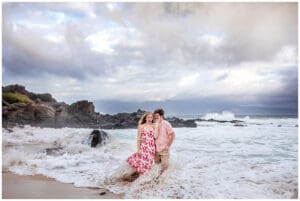 A loving couple embraces on a Maui beach during a romantic sunset photoshoot, with golden sand, gentle waves, and a breathtaking sky creating a dreamy atmosphere.