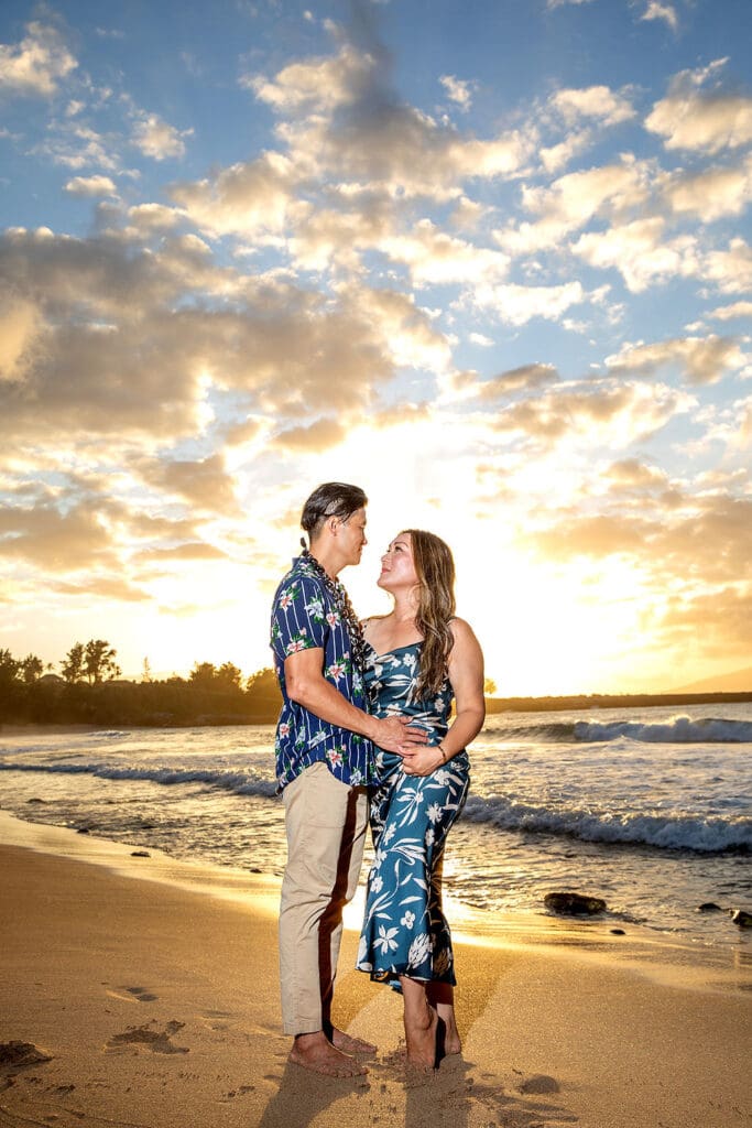 A loving couple embraces on a Maui beach during a romantic sunset photoshoot, with golden sand, gentle waves, and a breathtaking sky creating a dreamy atmosphere.