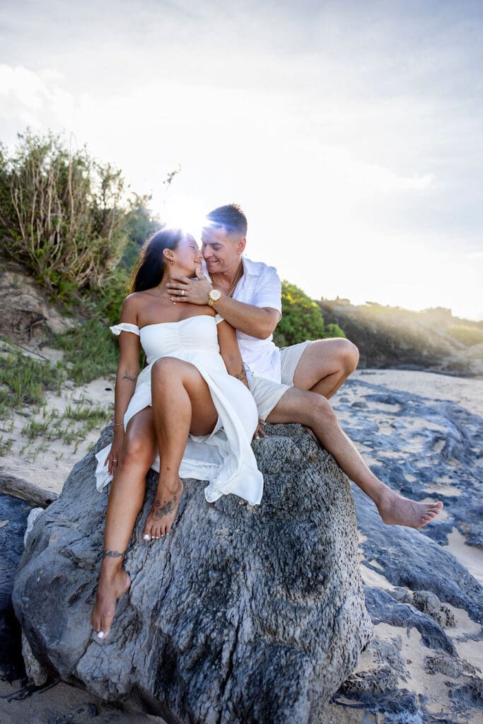 A loving couple embraces on a Maui beach during a romantic sunset photoshoot, with golden sand, gentle waves, and a breathtaking sky creating a dreamy atmosphere.