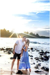 A loving couple embraces on a Maui beach during a romantic sunset photoshoot, with golden sand, gentle waves, and a breathtaking sky creating a dreamy atmosphere.