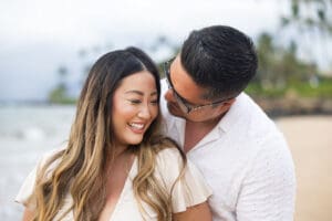 A loving couple embraces on a Maui beach during a romantic sunset photoshoot, with golden sand, gentle waves, and a breathtaking sky creating a dreamy atmosphere.