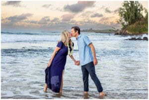 A loving couple embraces on a Maui beach during a romantic sunset photoshoot, with golden sand, gentle waves, and a breathtaking sky creating a dreamy atmosphere.