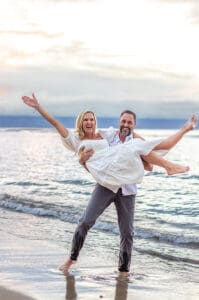 A loving couple embraces on a Maui beach during a romantic sunset photoshoot, with golden sand, gentle waves, and a breathtaking sky creating a dreamy atmosphere.